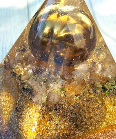 Pirámide grande de orgonita con bola metálica dorada sobre piezas de CITRINO